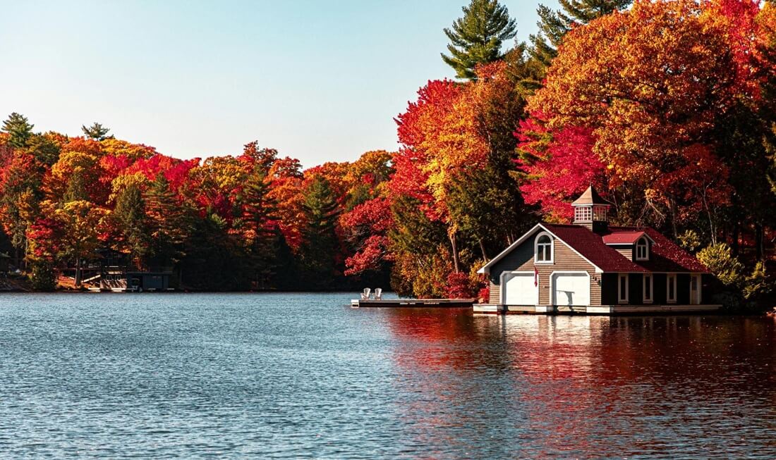Cottage with a boathouse on a lake surrounded by trees in autumn