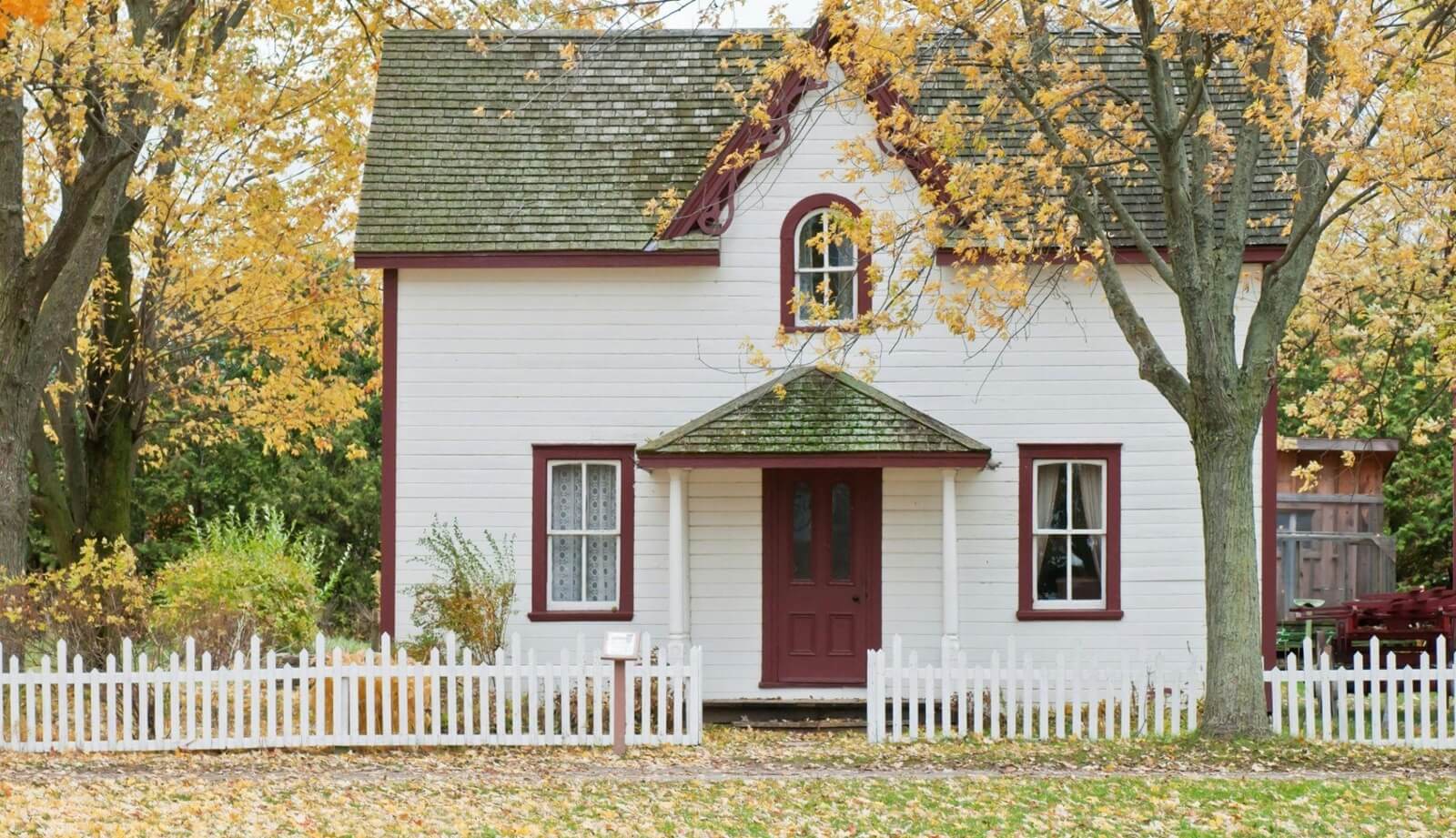 White cottage with red trim and a white picket fence in Ontario