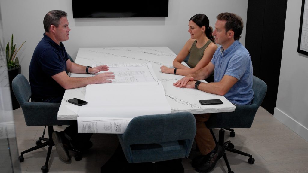 A couple meeting with contractor John DeCarli and looking at the blueprint of a home design