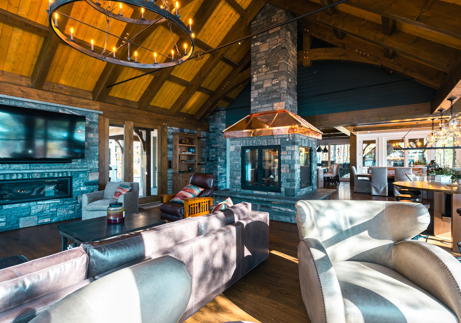 In-Depth and Contemplated Design: A Path to Efficient and Cost-Effective Home and Cottage Construction - A spacious, rustic living room with wooden beams and stone walls, featuring a fireplace, large TV, and cozy seating. The ceiling is vaulted, and sunlight streams through the windows, illuminating the elegant decor and furniture.